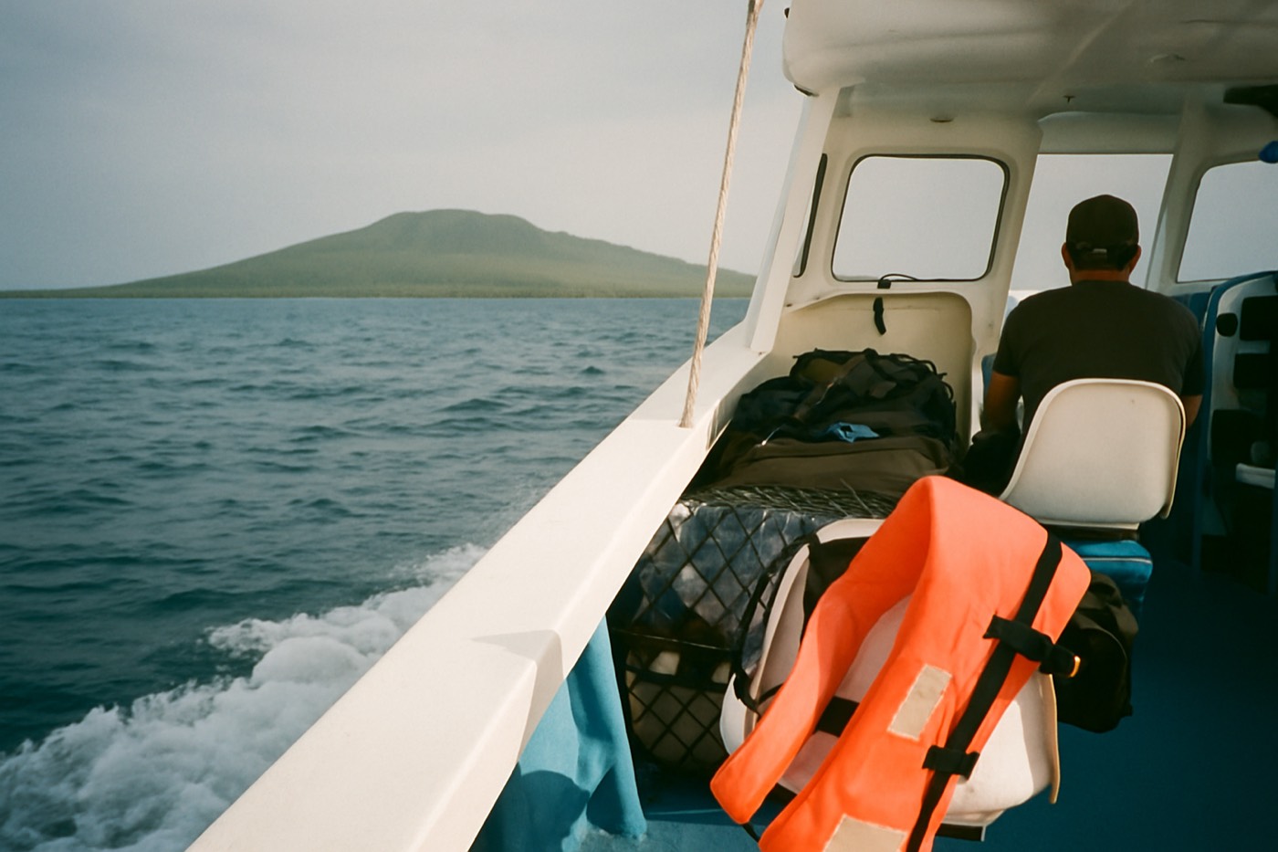 A public inter-island passenger boat crossing open water with a volcanic island low on the horizon