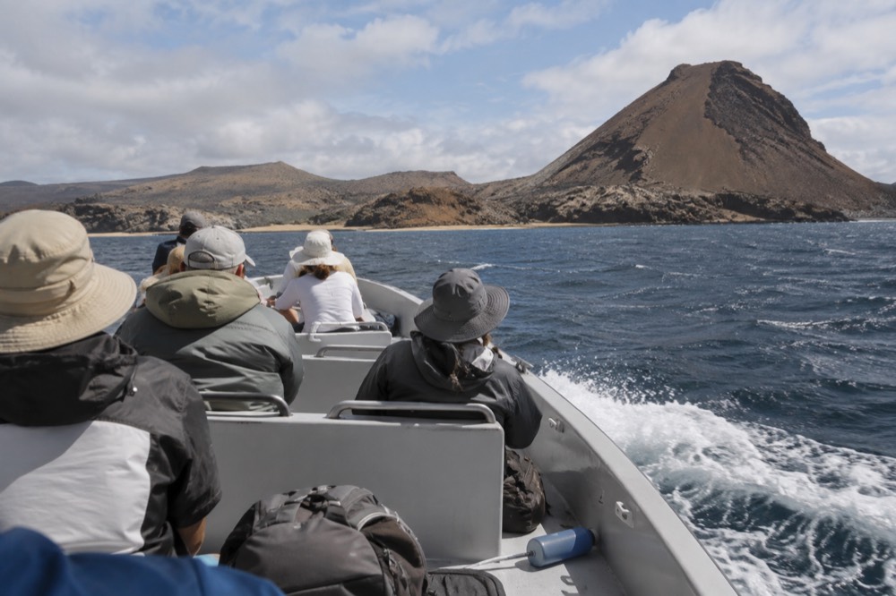 Midday crossing in the Galapagos Islands, Ecuador: a full day-tour boat pushes through a long chop toward Bartolome's stark cone, spray off the bow