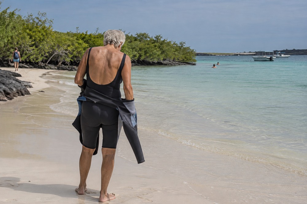 A senior snorkeller peels down a wetsuit at the calm shoreline of Las Bachas Beach, Galapagos Islands, Ecuador