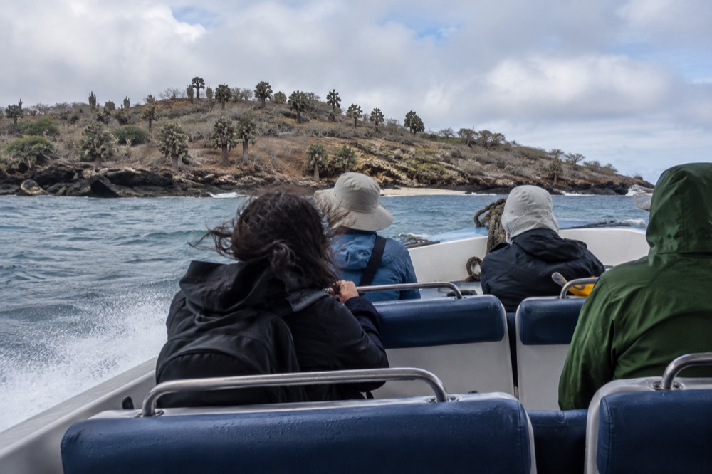 Inside an open fibreglass lancha crossing toward Santa Fe Island, Ecuador, cool-season wind and spray hitting fixed padded seats