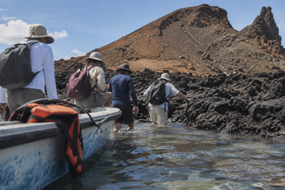 A small tour panga noses toward the lava landing on Bartolomé Island, Galapagos Islands, Ecuador, passengers stepping into shin-deep water at midday