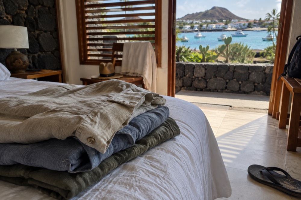 A folded stack of neutral linen and quick-dry shirts on a hotel bed in Puerto Ayora, Galapagos Islands, Ecuador